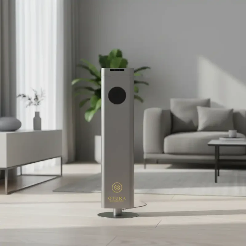 The Otura Essence freestanding tower scent diffuser in titanium aluminum, placed on a wooden floor in a bright, modern living room.